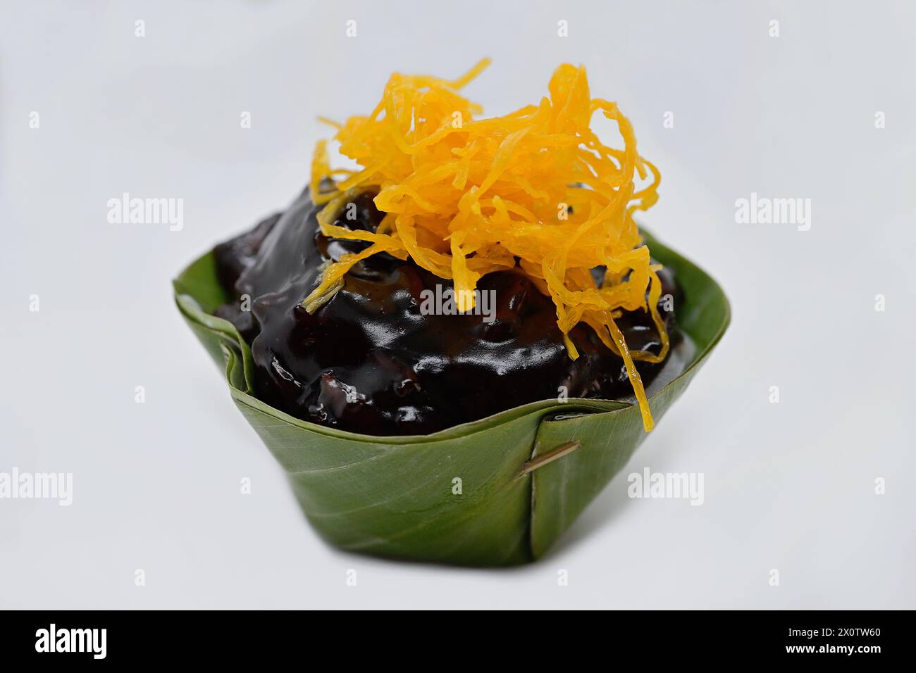 Gros plan d'un dessert thaïlandais Khanom Tako à l'envers, avec du riz gluant noir et des lambeaux de jaune d'oeuf doré doux (foi Thong) dans une coupe à feuilles de pandan Banque D'Images