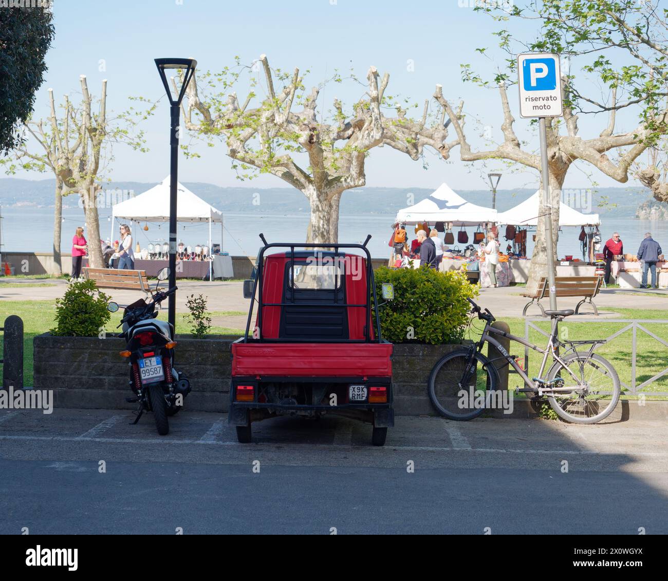 Véhicule APE dans un parking avec des arbres inhabituels et des étals de marché à Marta surplombant le lac de Bolsena, province de Viterbo, région du Latium, Italie. 13 avril 2024 Banque D'Images