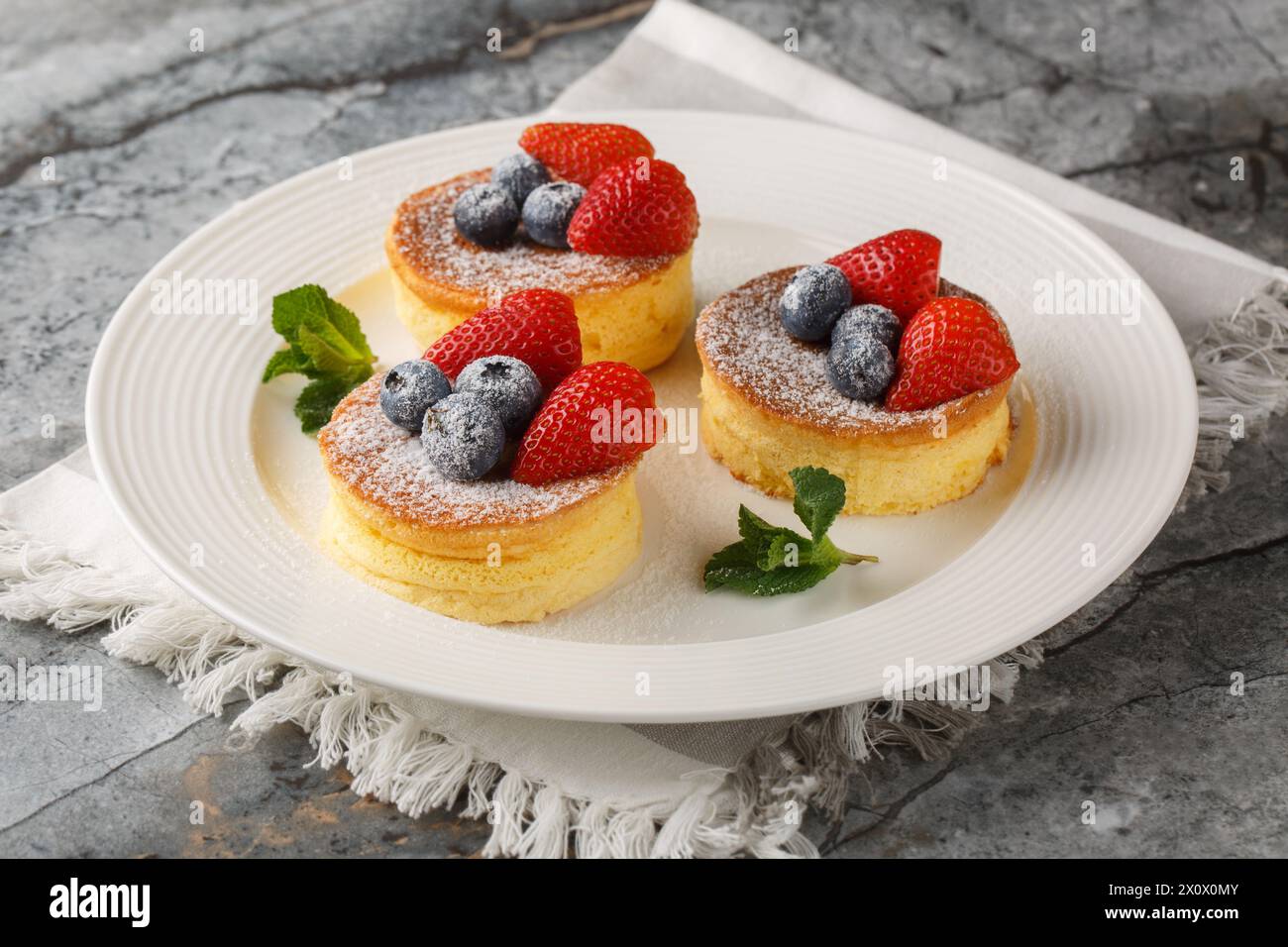 Crêpes japonaises molles à la fraise et aux myrtilles saupoudrées de sucre en poudre gros plan sur une assiette sur la table. Horizontal Banque D'Images