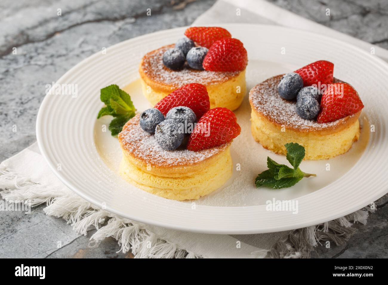 Crêpes japonaises molles aux baies saupoudrées de sucre en poudre gros plan sur une assiette sur la table. Horizontal Banque D'Images