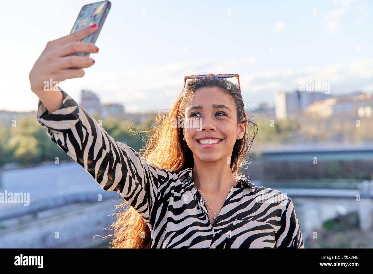Selfie de femme latina heureuse et joyeuse dans des vêtements décontractés. Fille hispanique excitée avec un téléphone intelligent souriant et prenant une photo Banque D'Images