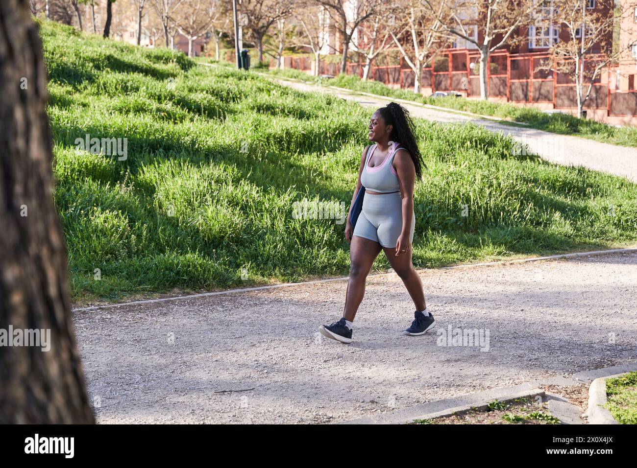 Jeune femme afro-américaine en vêtements de sport marchant à travers un parc de la ville sur son chemin à la salle de gym pour s'entraîner. Banque D'Images