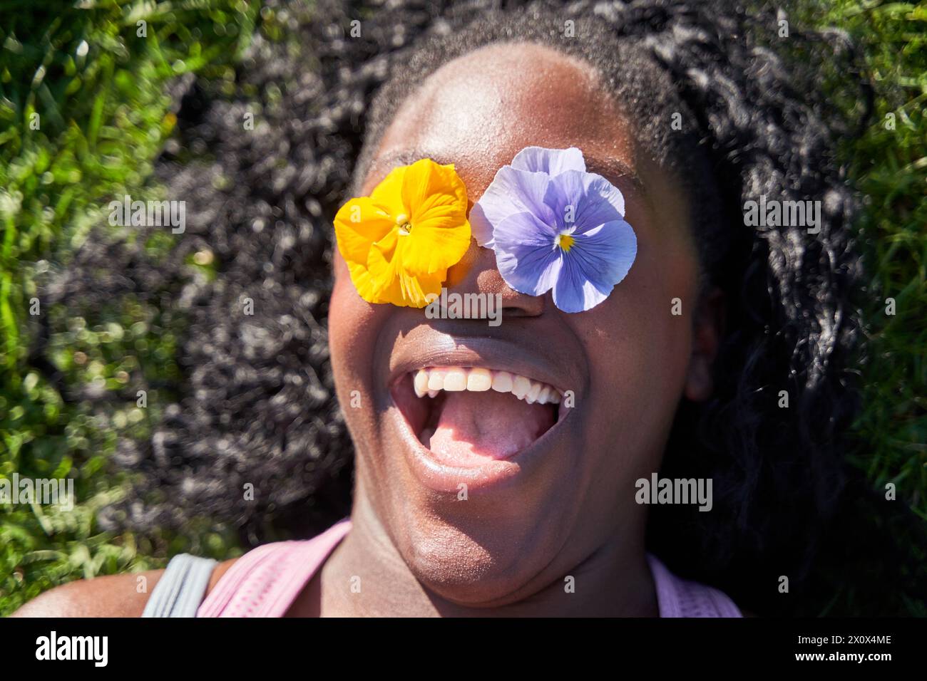 Ludique positive afro-américaine femme couvre les yeux avec deux fleurs, aime le printemps, fleurs fraîches, s'amuse, Banque D'Images