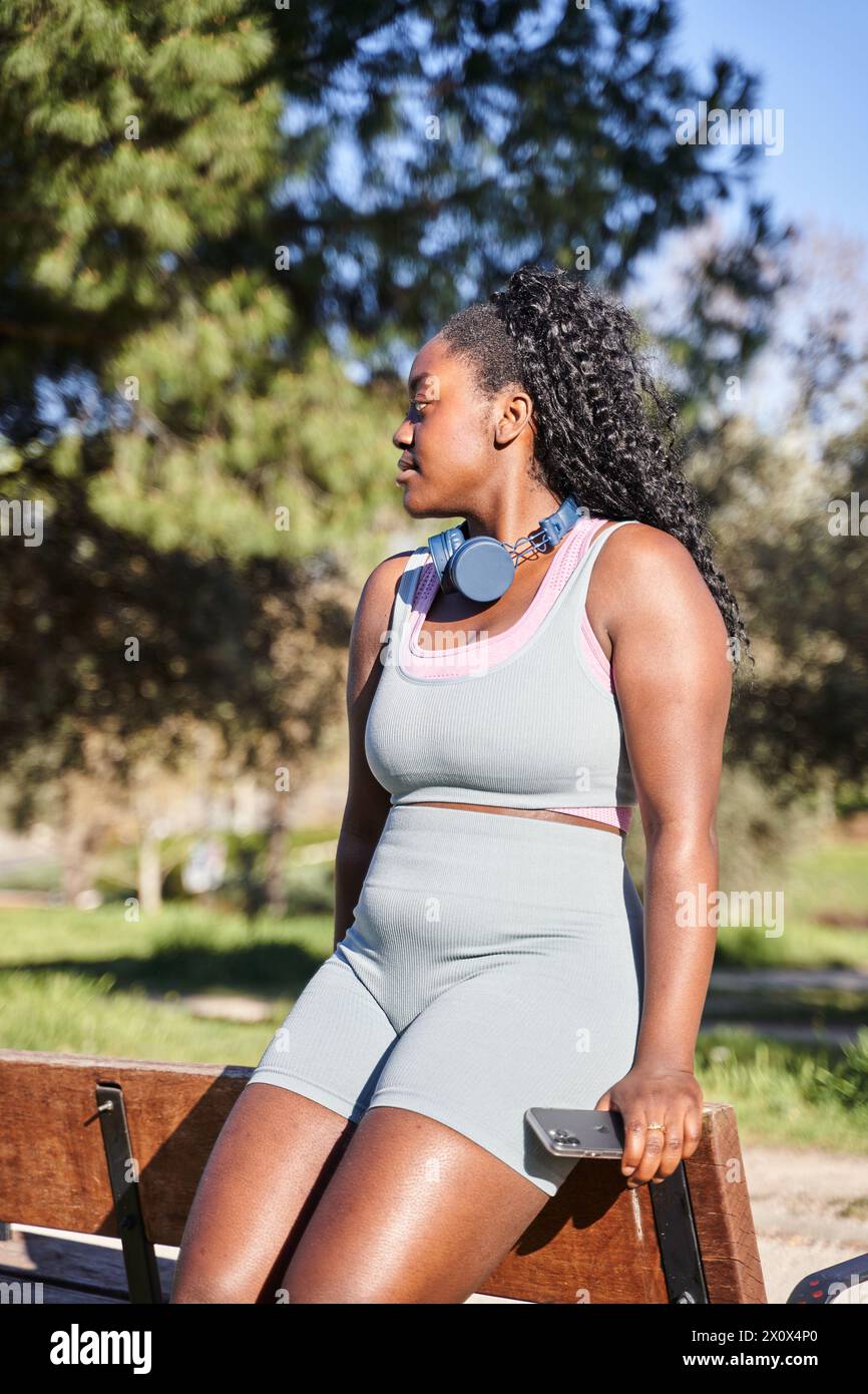 jeune femme afro-américaine assise sur un banc pendant une pause en entraînement en plein air. femme sinueuse sans complexes. Banque D'Images