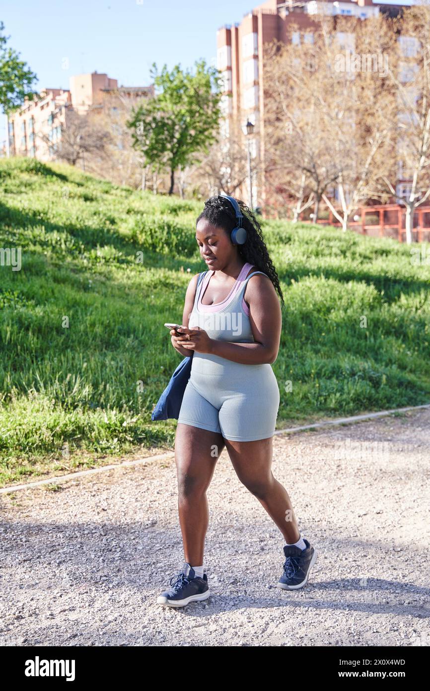 attrayant femme afro-américaine courbée marchant dans des vêtements de sport tout en utilisant son smartphone Banque D'Images