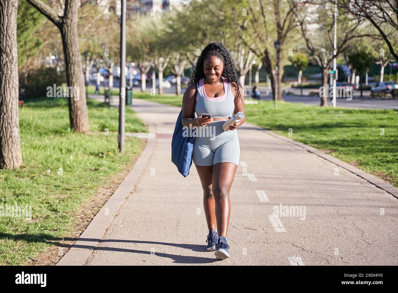 Athlète féminine marchant après un entraînement en plein air. Femme afro-américaine utilisant son smartphone Banque D'Images