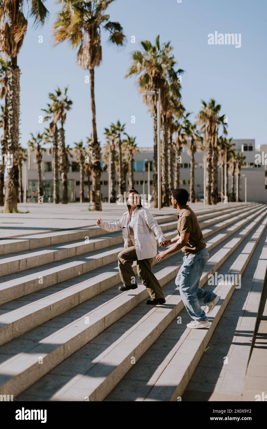 Les jeunes couples se réunissent joyeusement sur les marches d'une promenade bordée de palmiers dans le paysage urbain animé de Barcelonas Banque D'Images