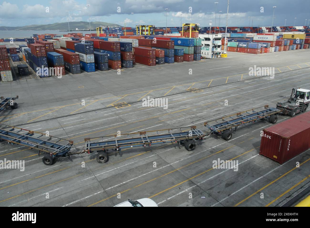 Wagon de marchandises avec véhicules remorqueurs ou voie de livraison ressemblant à un train passant devant des conteneurs arrimés dans le terminal portuaire de Kingston. Banque D'Images