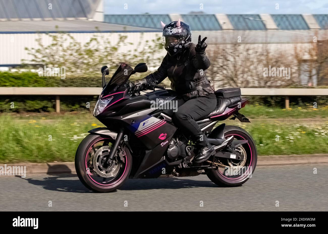 Milton Keynes, UK- 14 avril 2024 : 2014 Yamaha XJ montée par une motard dame avec des cornes roses sur son casque Banque D'Images