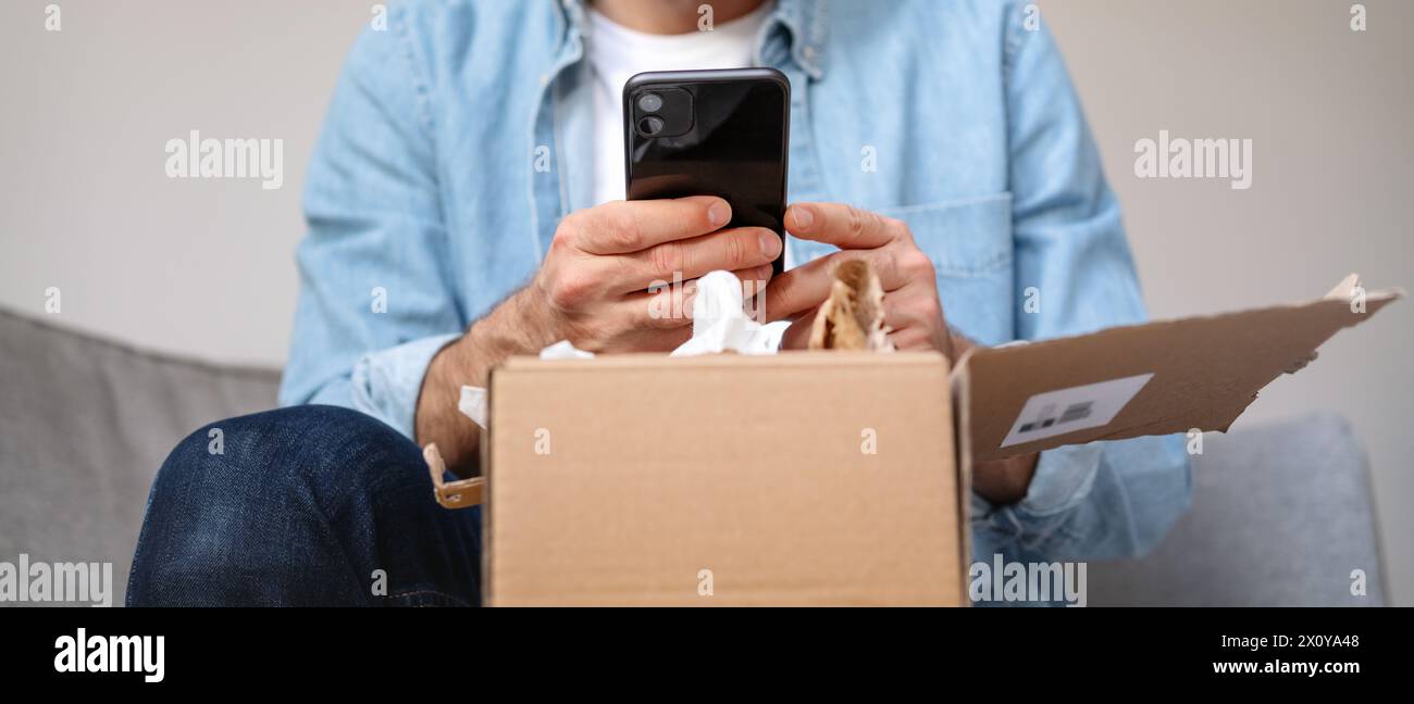 Homme déballant un paquet et prenant une photo de son achat, commande internet. Personne partageant des commentaires avec la boutique en ligne à l'aide de son smartphone. Banque D'Images