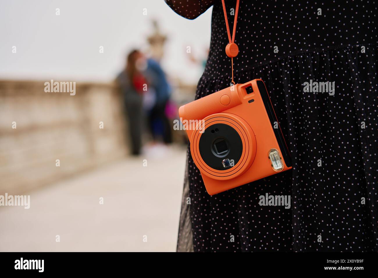 Femme tenant la caméra instantanée orange. Touriste capture des souvenirs pendant le voyage avec l'appareil photo vintage Banque D'Images