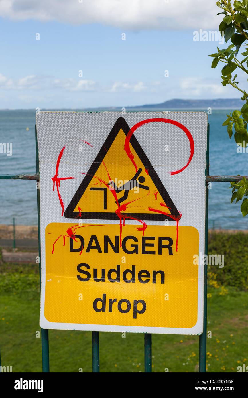 Danger, signe de route soudaine chute contre l'herbe verte et fond de mer sur une journée nuageuse Banque D'Images