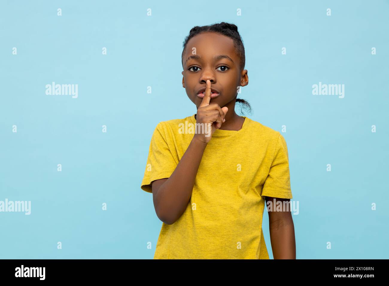 Petit garçon sérieux à la peau foncée montrant un geste de silence Banque D'Images