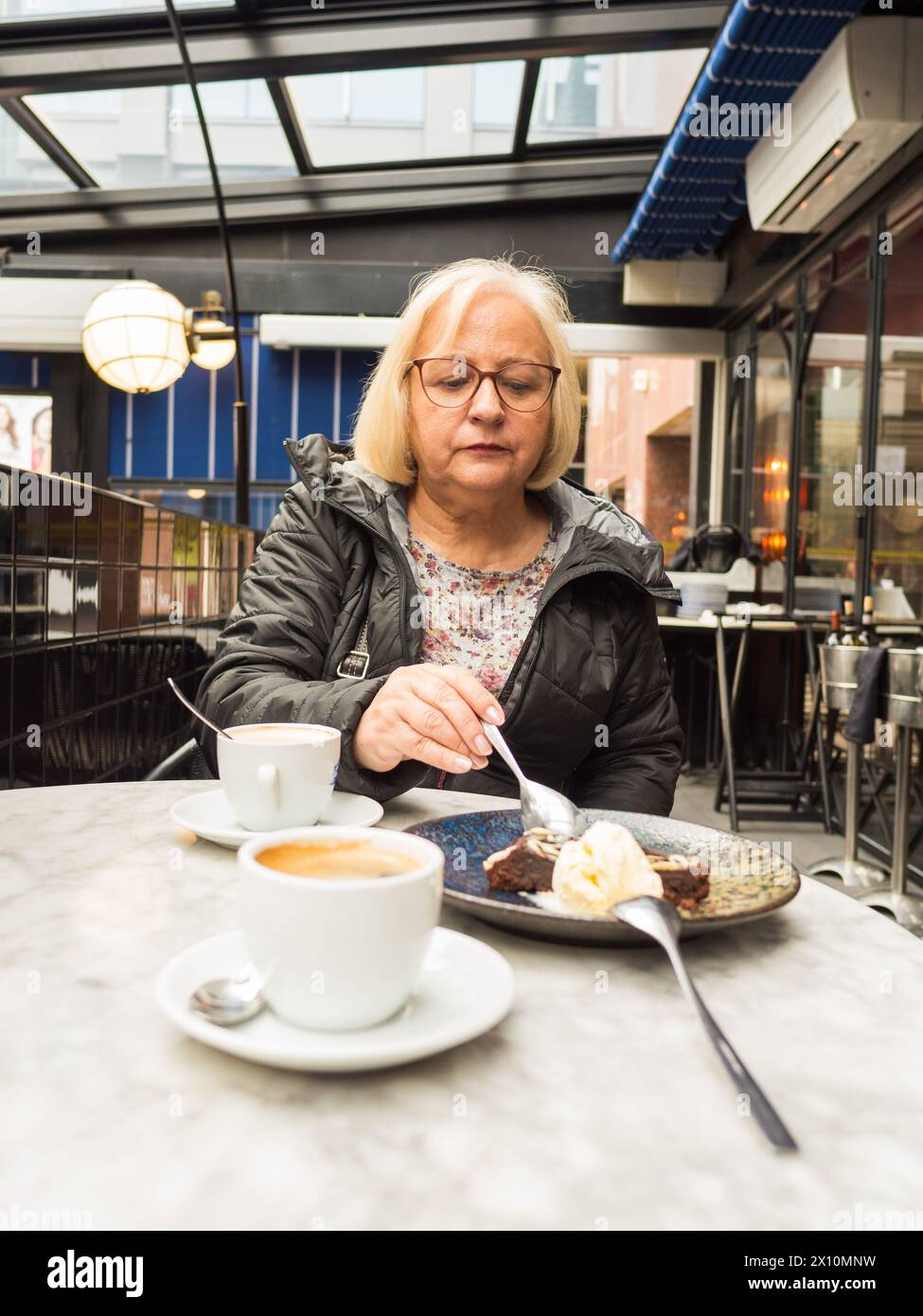 Blonde senior avec des verres partage le dessert sucré brownie avec inquiétude dans un café Banque D'Images