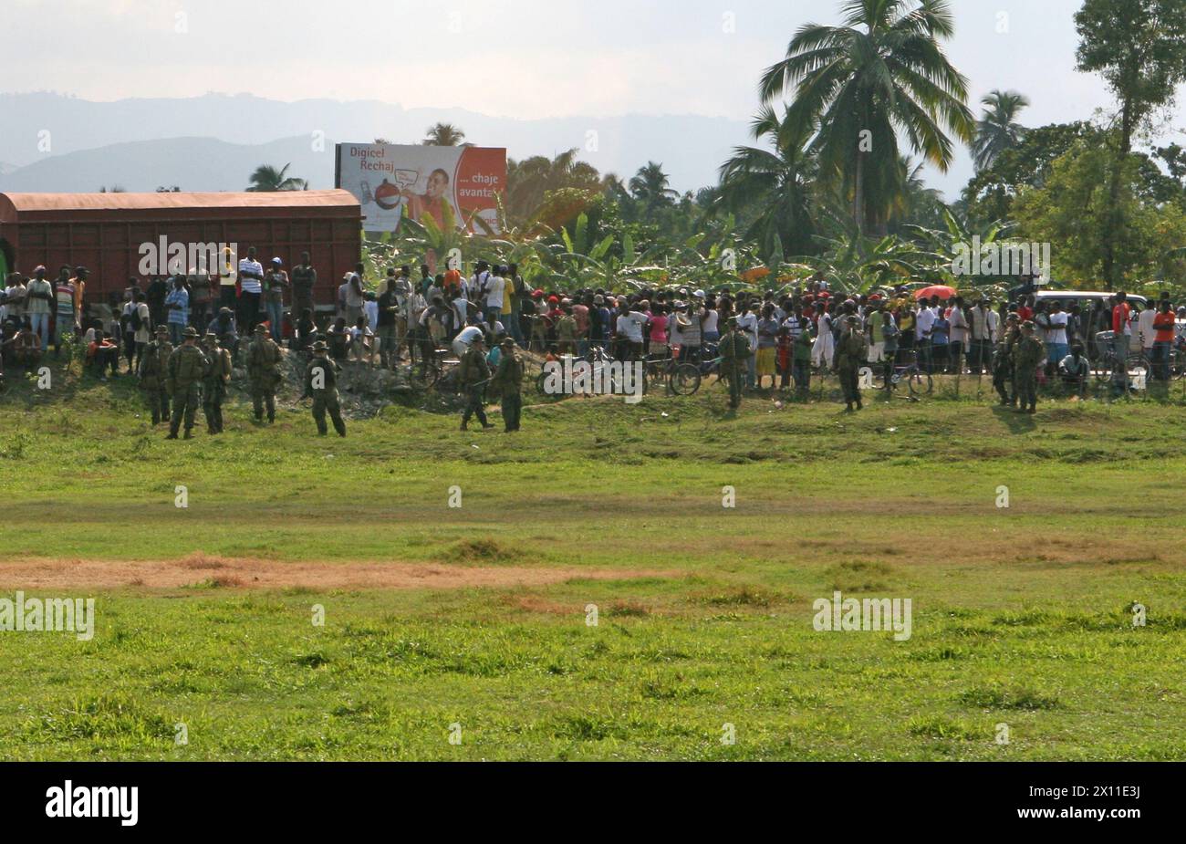 Les Haïtiens locaux se rassemblent autour de la zone d'atterrissage des hélicoptères, sécurisée par des Marines de la Compagnie Lima, de l'équipe de débarquement du bataillon, du 3e bataillon, du 2e régiment de Marines, de la 22e unité expéditionnaire des Marines à Léogane, Haïti, le 20 janvier 2010. Banque D'Images