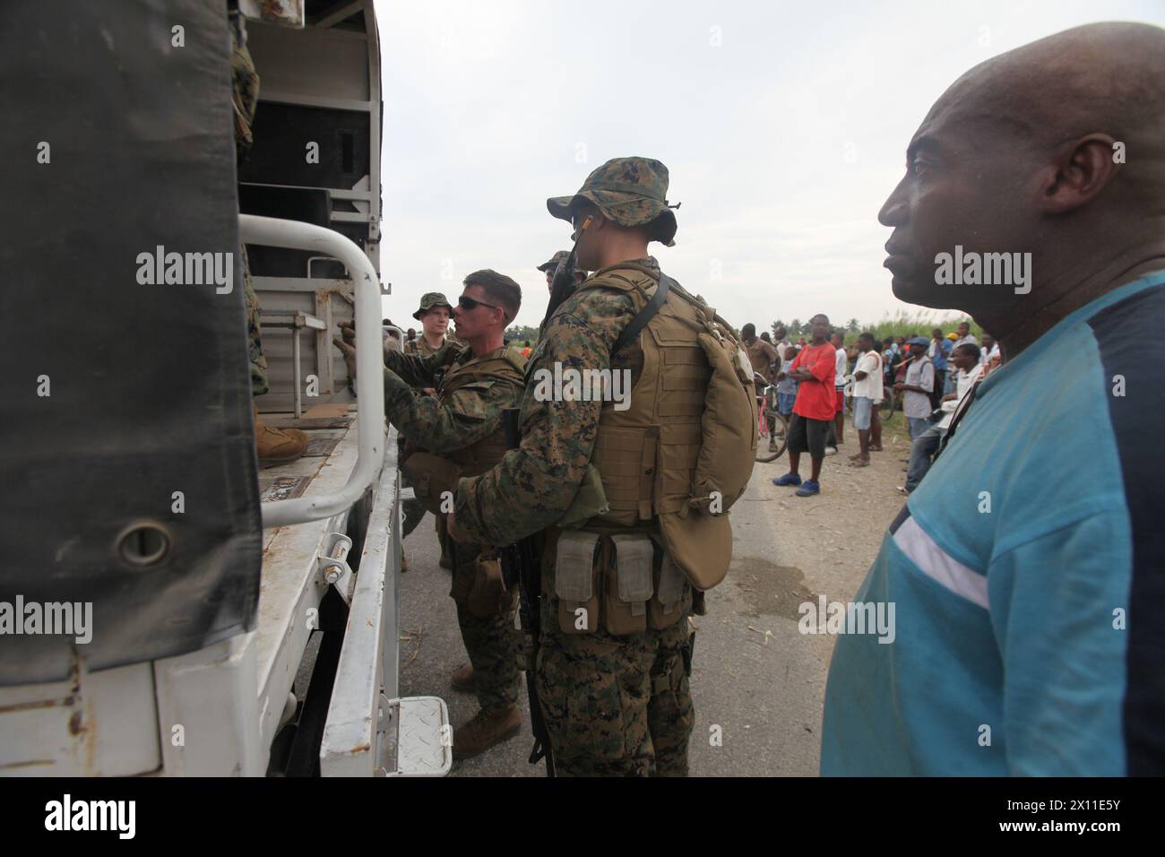 Un haïtien local regarde alors que des Marines avec l'équipe de débarquement du bataillon, le 3e bataillon, le 2e régiment de Marines, la 22e unité expéditionnaire des Marines, chargent un véhicule des Nations Unies à proximité lors d'une mission d'approvisionnement en nourriture et en eau à Léogane, Haïti, le 19 janvier 2010. Banque D'Images