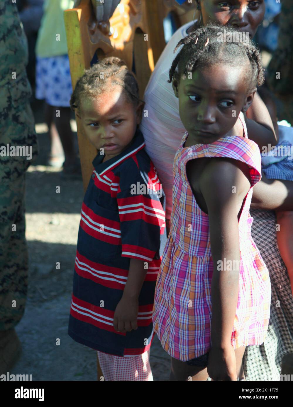 Deux filles haïtiennes se tiennent tranquillement debout alors que d'autres habitants reçoivent des soins médicaux de cadavres avec l'équipe de débarquement du bataillon, le 3e bataillon, le 2e régiment de Marines, la 22e unité expéditionnaire des Marines, lors d'une mission d'aide médicale à Dano, Haïti, le 28 janvier 2010. La mission médicale faisait partie des efforts continus de la 22e MEU pour fournir des secours à l'appui de l'opération réponse unifiée. Banque D'Images