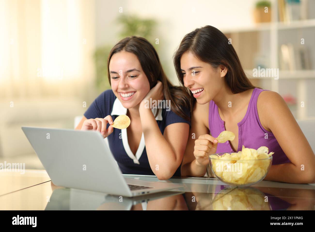 Deux amis heureux regardant un film sur ordinateur portable manger un snack assis à la maison Banque D'Images