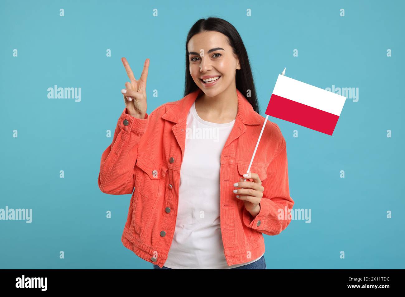 Heureuse jeune femme avec le drapeau de la Pologne montrant V-signe sur fond bleu clair Banque D'Images