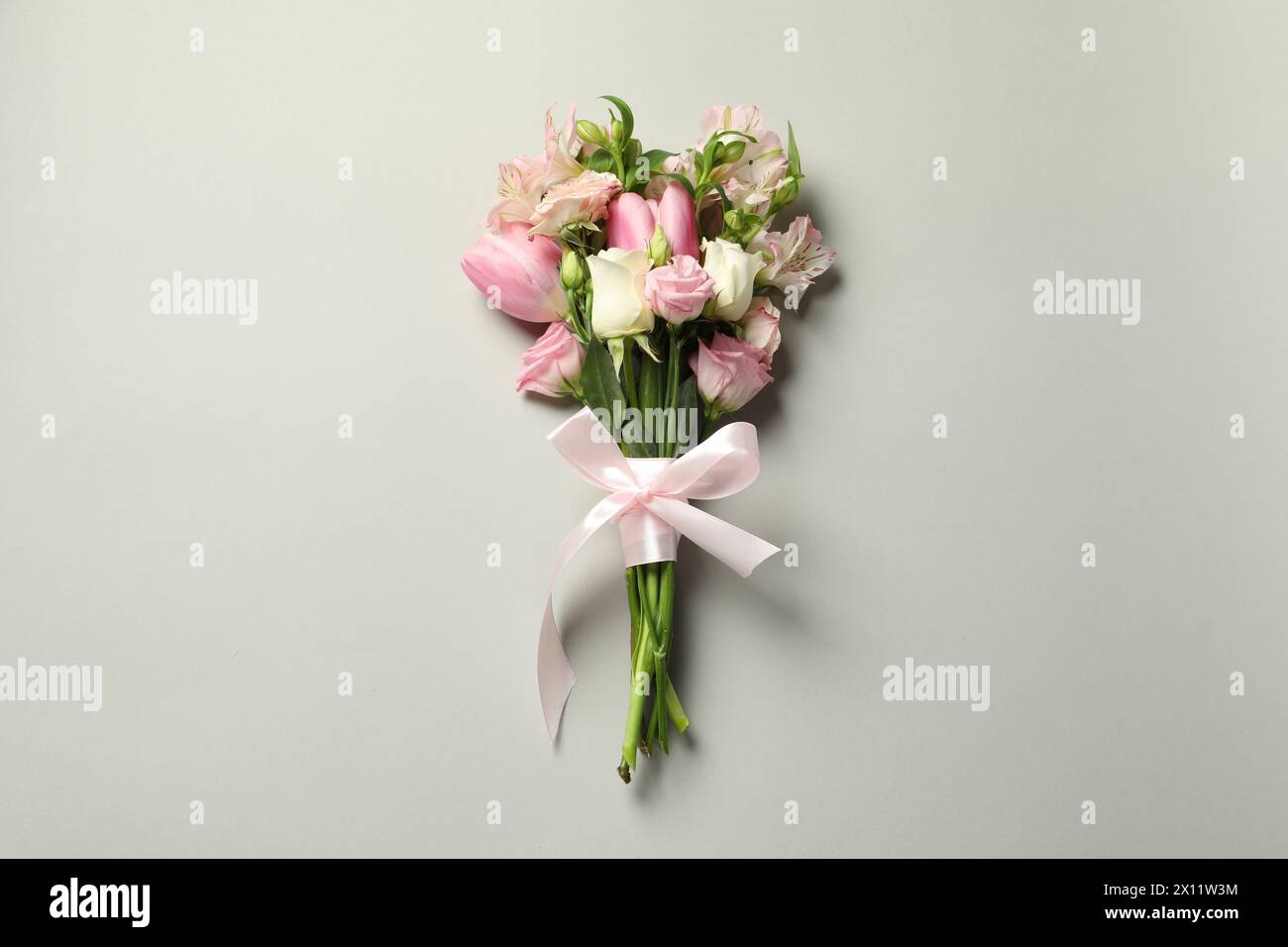 Bonne fête des mères. Bouquet de belles fleurs attachées avec ruban rose sur fond gris clair, vue de dessus Banque D'Images