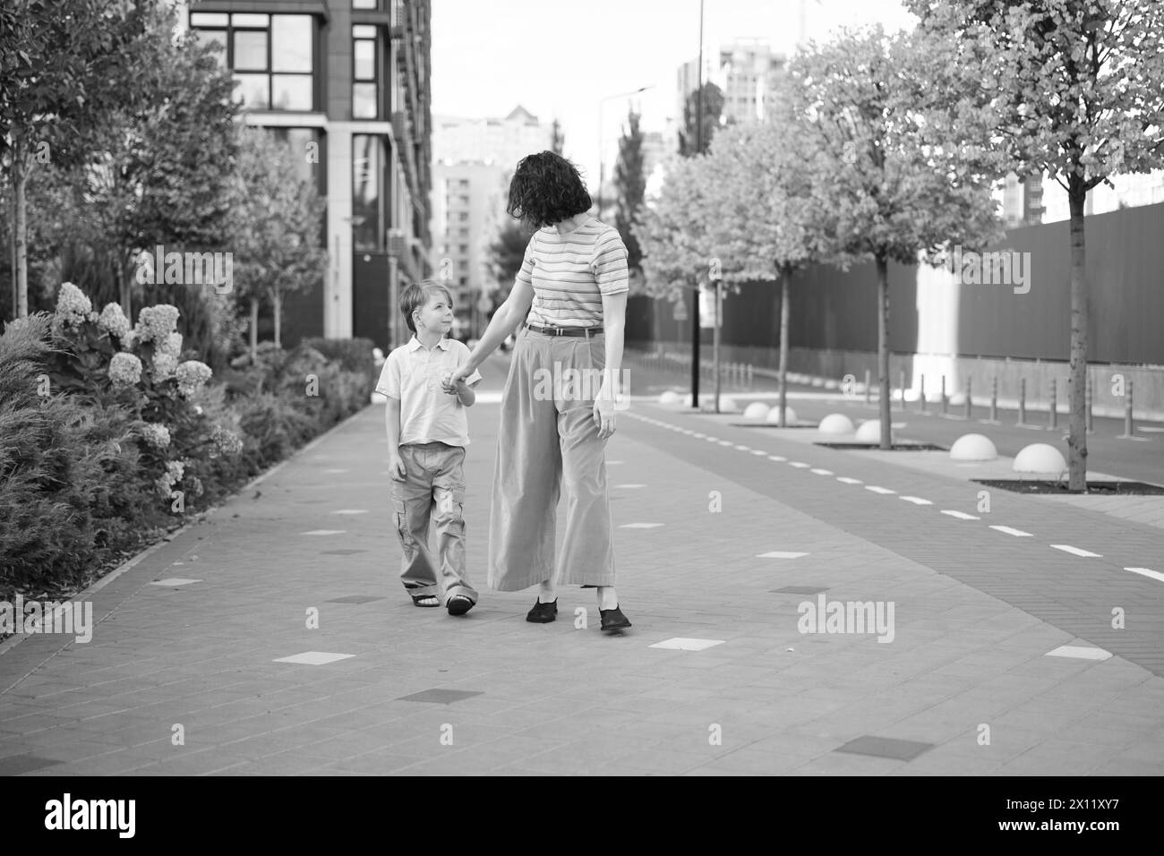 Caucasien jeune belle mère heureuse et mignon petit fils marchant dans la rue et se regardant les uns les autres. Femme et petit garçon souriant, parlant et ayant des vacances. Photo de haute qualité Banque D'Images