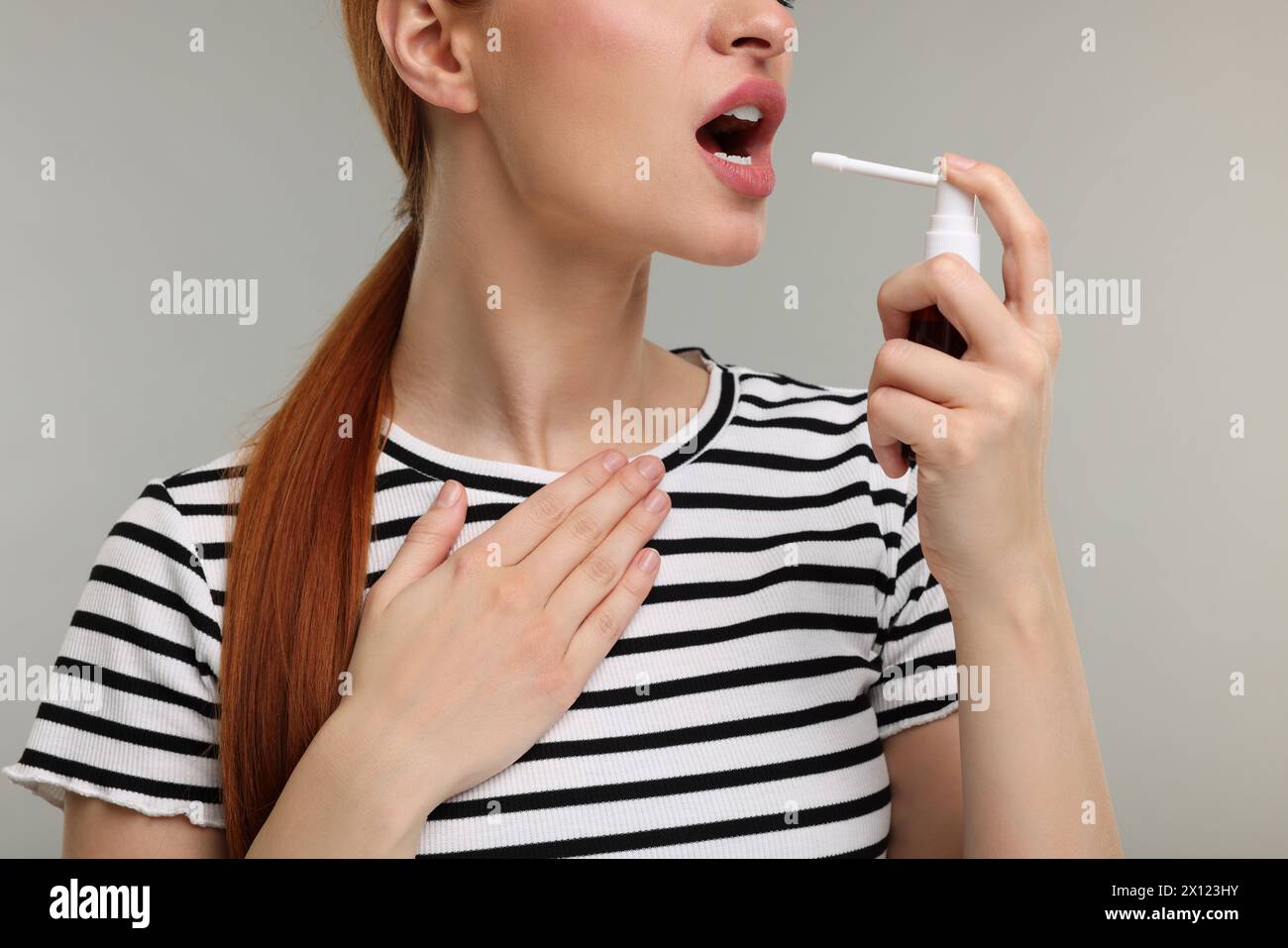 Jeune femme utilisant le spray de gorge sur fond gris, gros plan Banque D'Images