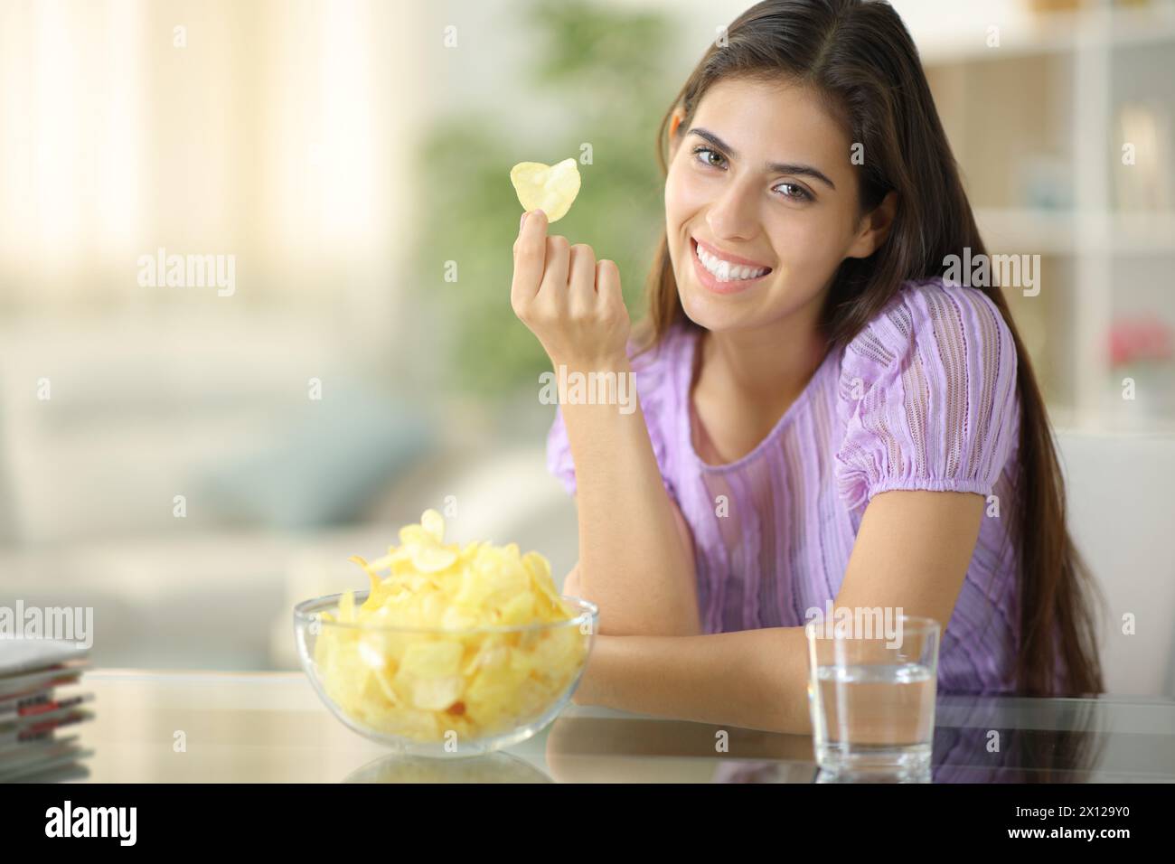 Femme heureuse te regarde tenant des chips à la maison Banque D'Images