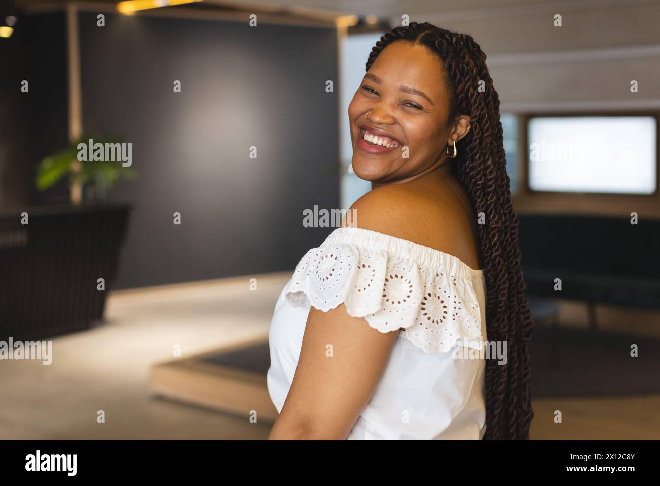 Une jeune femme biraciale sourit dans un bureau d'affaires moderne avec un espace de copie Banque D'Images