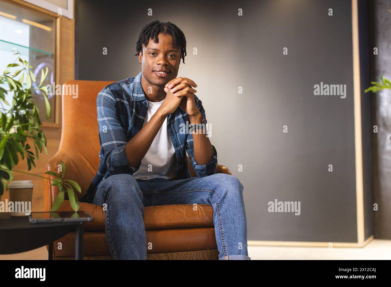 Homme afro-américain assis dans un bureau d'affaires moderne, les mains serrées, regardant la caméra Banque D'Images