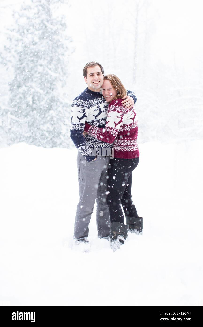 Couple marié dans Christmas Sweaters Hug dans les chutes de neige Banque D'Images