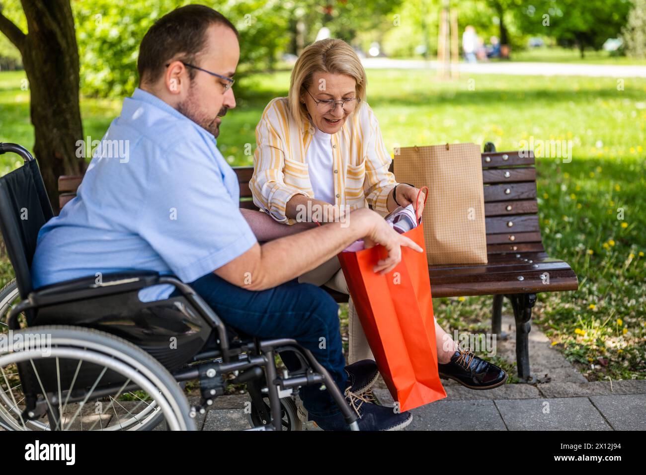 L'homme en fauteuil roulant passe du temps avec sa mère dans le parc. Ils parlent après avoir fait du shopping. Banque D'Images