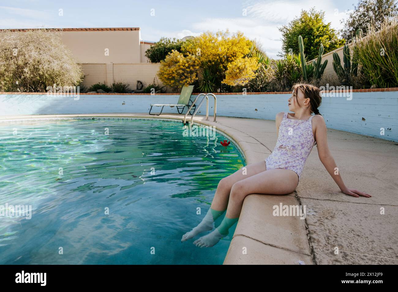 Tween Girl assis sur le côté de la piscine regardant loin Banque D'Images