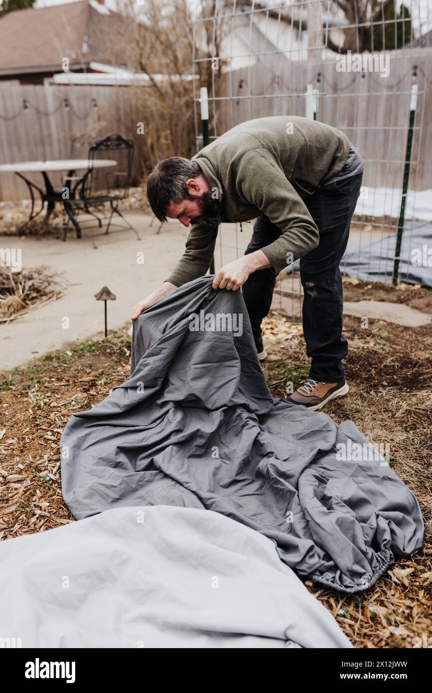 L'homme couvre les plantes avec un drap de lit pour les protéger des tempêtes de neige Banque D'Images