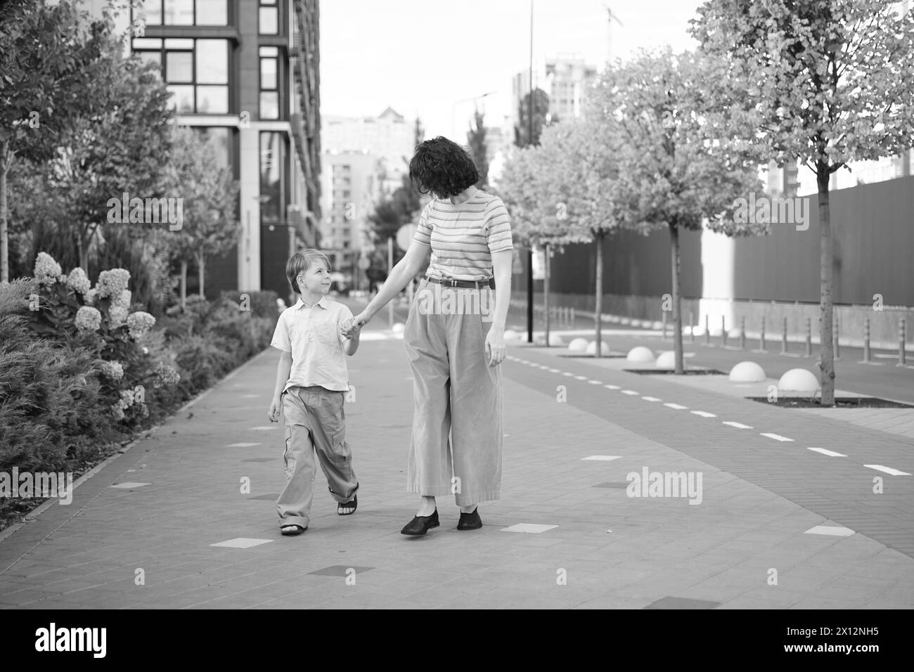 Caucasien jeune belle mère heureuse et mignon petit fils marchant dans la rue et se regardant les uns les autres. Femme et petit garçon souriant, parlant et ayant des vacances. Photo de haute qualité Banque D'Images
