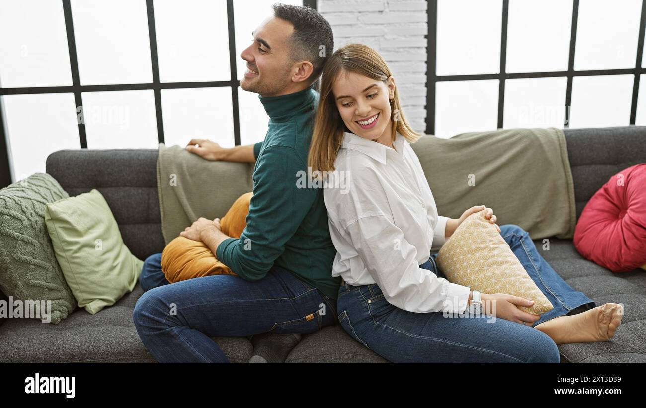 Un couple souriant est assis dos à dos dans un salon confortable, exsudant l'amour et la compagnie dans un cadre confortable à la maison. Banque D'Images