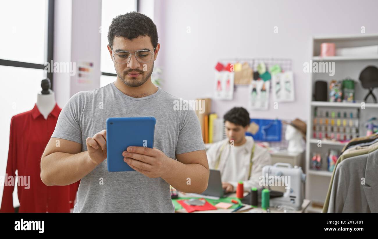 Deux hommes travaillant dans un tailleur, l'un utilisant une tablette et l'autre cousant. Banque D'Images