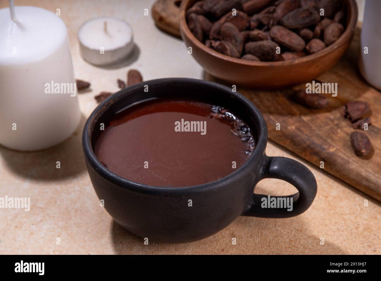 Boisson cérémonielle au cacao. Chocolat cérémonial chaud dans une tasse noire avec des fèves de cacao. Mains de femme tenant une tasse de cacao. Préparation de boisson au chocolat biologique saine Banque D'Images