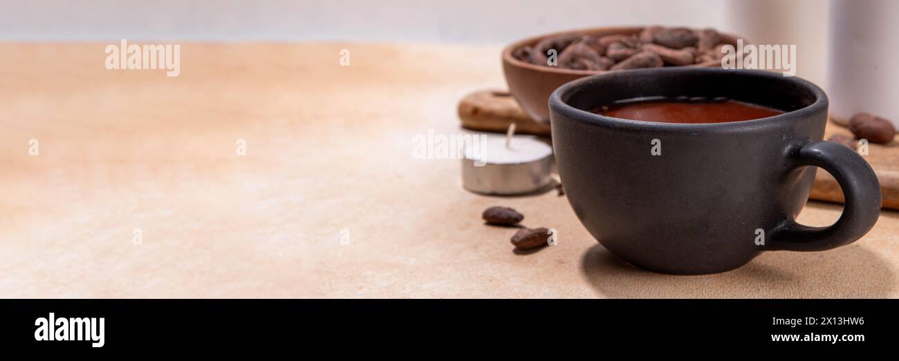 Boisson cérémonielle au cacao. Chocolat cérémonial chaud dans une tasse noire avec des fèves de cacao. Mains de femme tenant une tasse de cacao. Préparation de boisson au chocolat biologique saine Banque D'Images