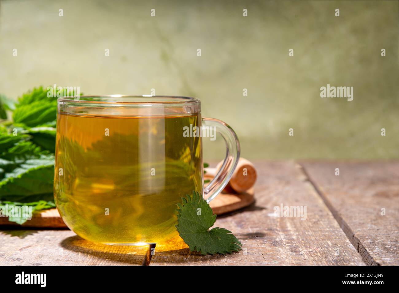Boisson végétale chaude au thé d'ortie dans une tasse en verre transparent. Tisane naturelle biologique sans caféine, faite avec des feuilles d'ortie crues biologiques. Alternative Her Banque D'Images