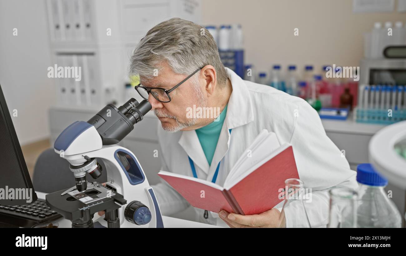 Scientifique mature utilisant le microscope dans le laboratoire à côté de l'ordinateur tout en tenant le cahier Banque D'Images