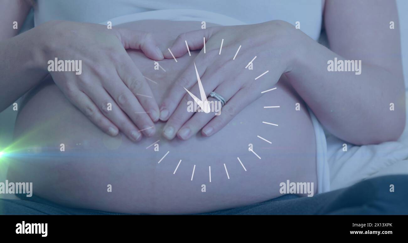 Horloge avec des mains en mouvement rapide sur une femme caucasienne enceinte heureuse faisant des mains de coeur sur le ventre Banque D'Images