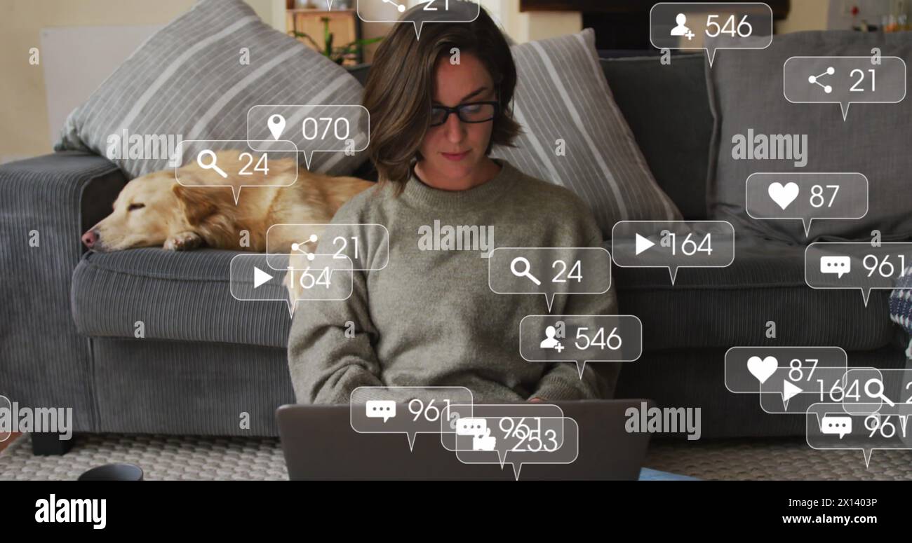 Icônes numériques sur les bulles de parole contre la femme caucasienne utilisant un ordinateur portable tandis que le chien dort sur le canapé Banque D'Images