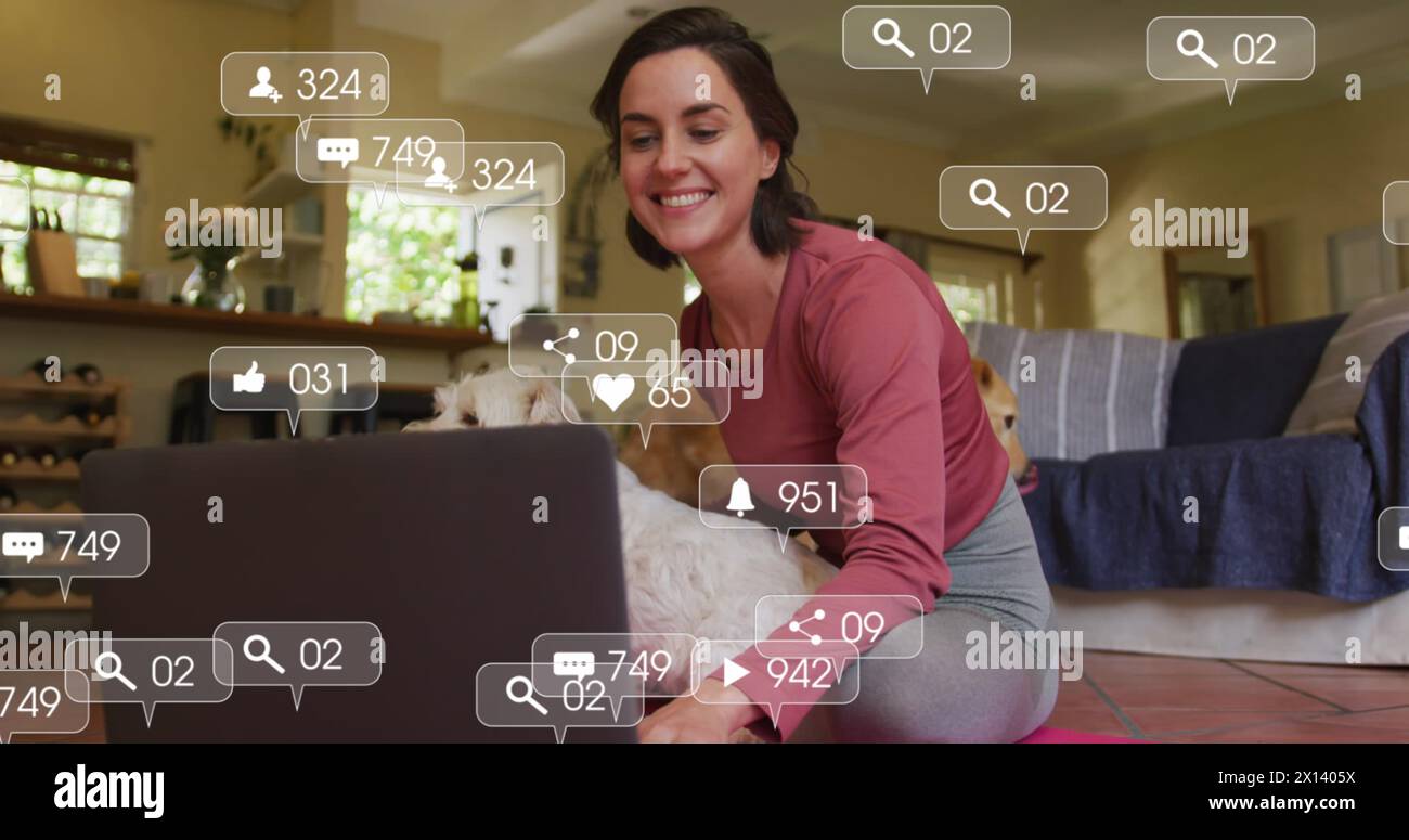 Icônes numériques sur les bulles de parole contre la femme caucasienne assise avec son chien à l'aide d'un ordinateur portable à la maison Banque D'Images