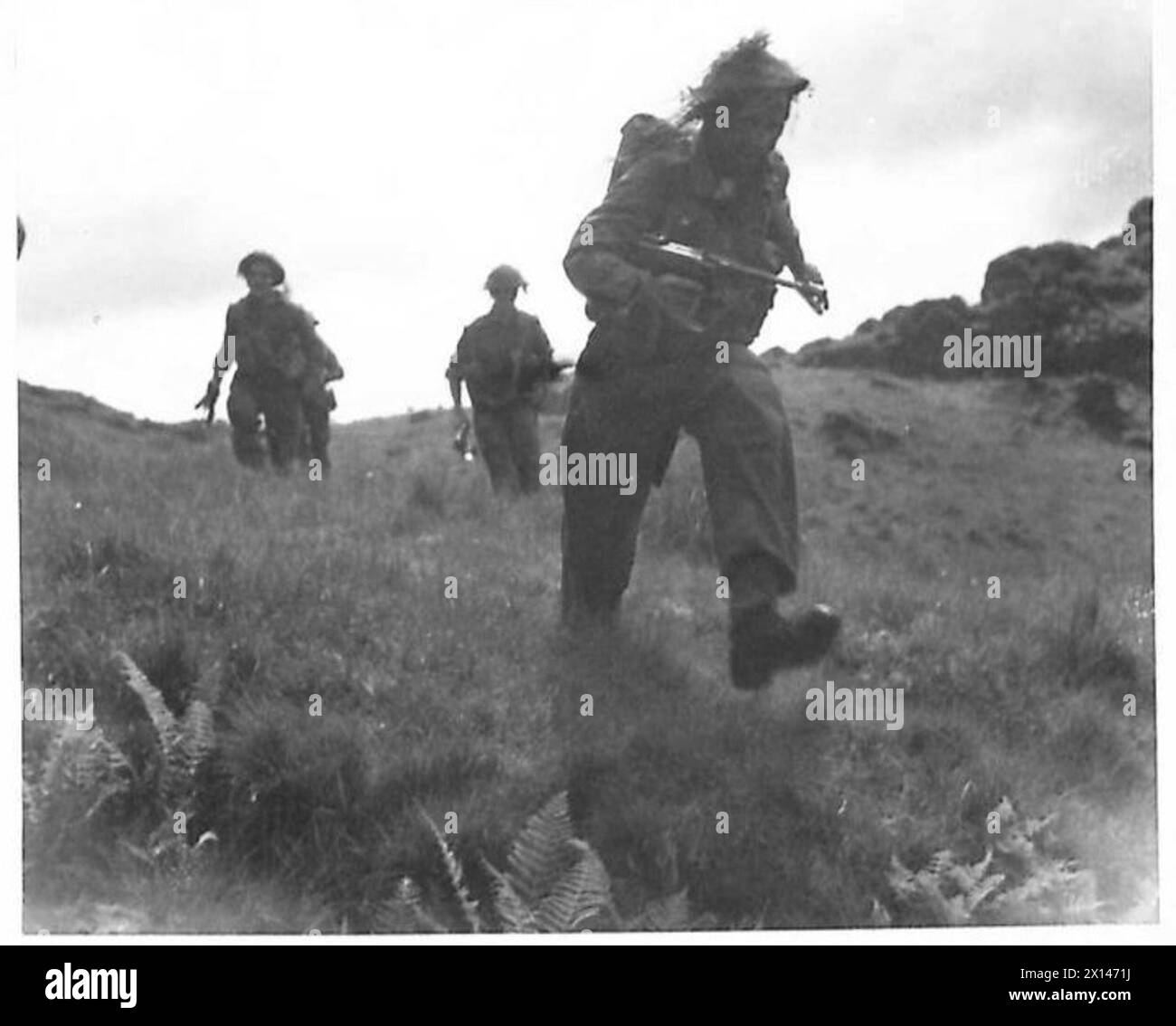 Un soldat de l'armée britannique avec un casque en acier camouflé et le visage noirci mène un assaut sur une position ennemie simulée pendant l'entraînement à l'école de bataille. Banque D'Images