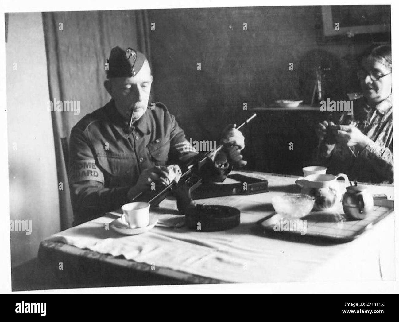 Un sergent de la Home Guard polit son arme Tommy avant de quitter la maison pour rejoindre un défilé, préparant son arme pour l'exposition et la préparation. Banque D'Images