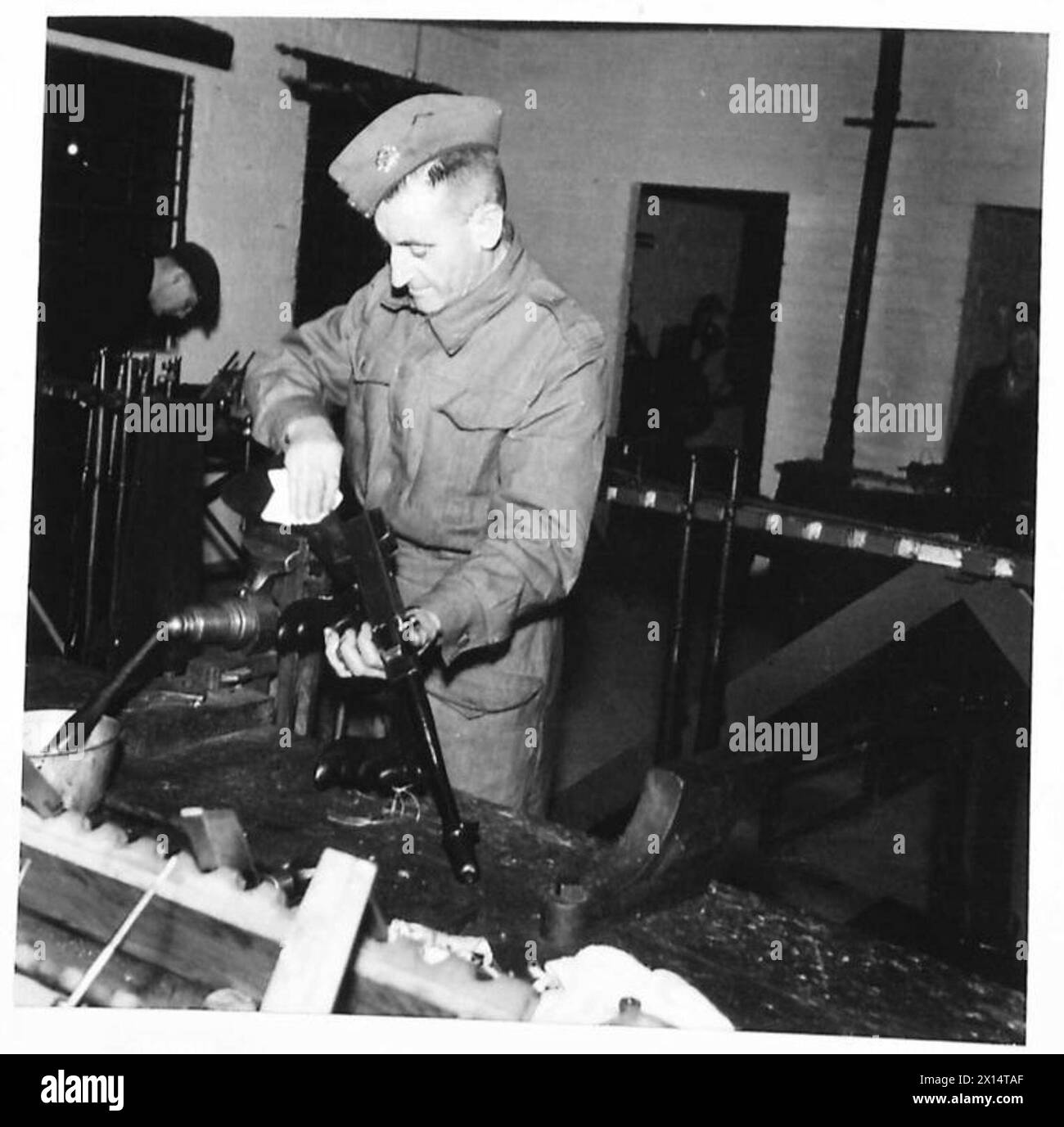 Un instructeur de formation aux armes manipule un pistolet Tommy dans un atelier du Royal Electrical and Mechanical Engineers, démontrant les procédures de maintenance et de fonctionnement. Banque D'Images