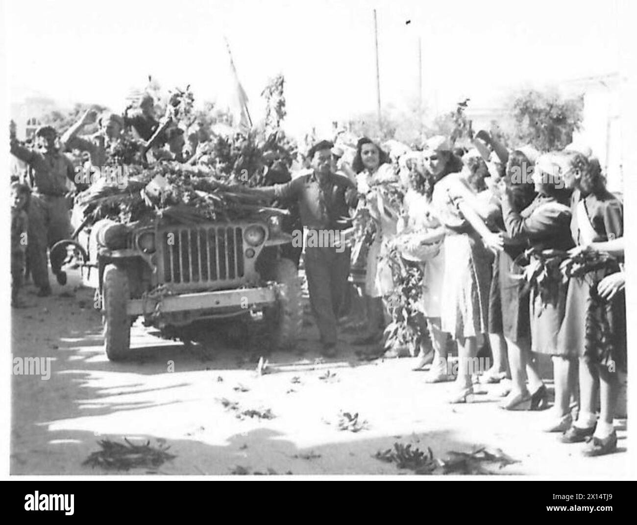Les troupes britanniques entrent à Corinthe lorsque des citoyens, y compris des membres de l'E.L.A.S., bordent les rues de guirlandes de fleurs pendant qu'une jeep passe. Banque D'Images
