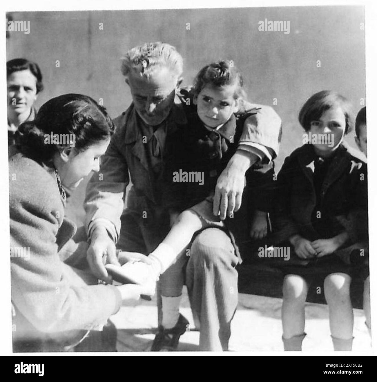 Une femme aide un enfant grec à essayer des chaussures distribuées par la Croix-Rouge, démontrant l'aide humanitaire fournie sous la supervision de l'armée britannique en Grèce. Banque D'Images Une femme aide un enfant grec à essayer des chaussures distribuées par la Croix-Rouge, démontrant l'aide humanitaire fournie sous la supervision de l'armée britannique en Grèce. Banque D'Images