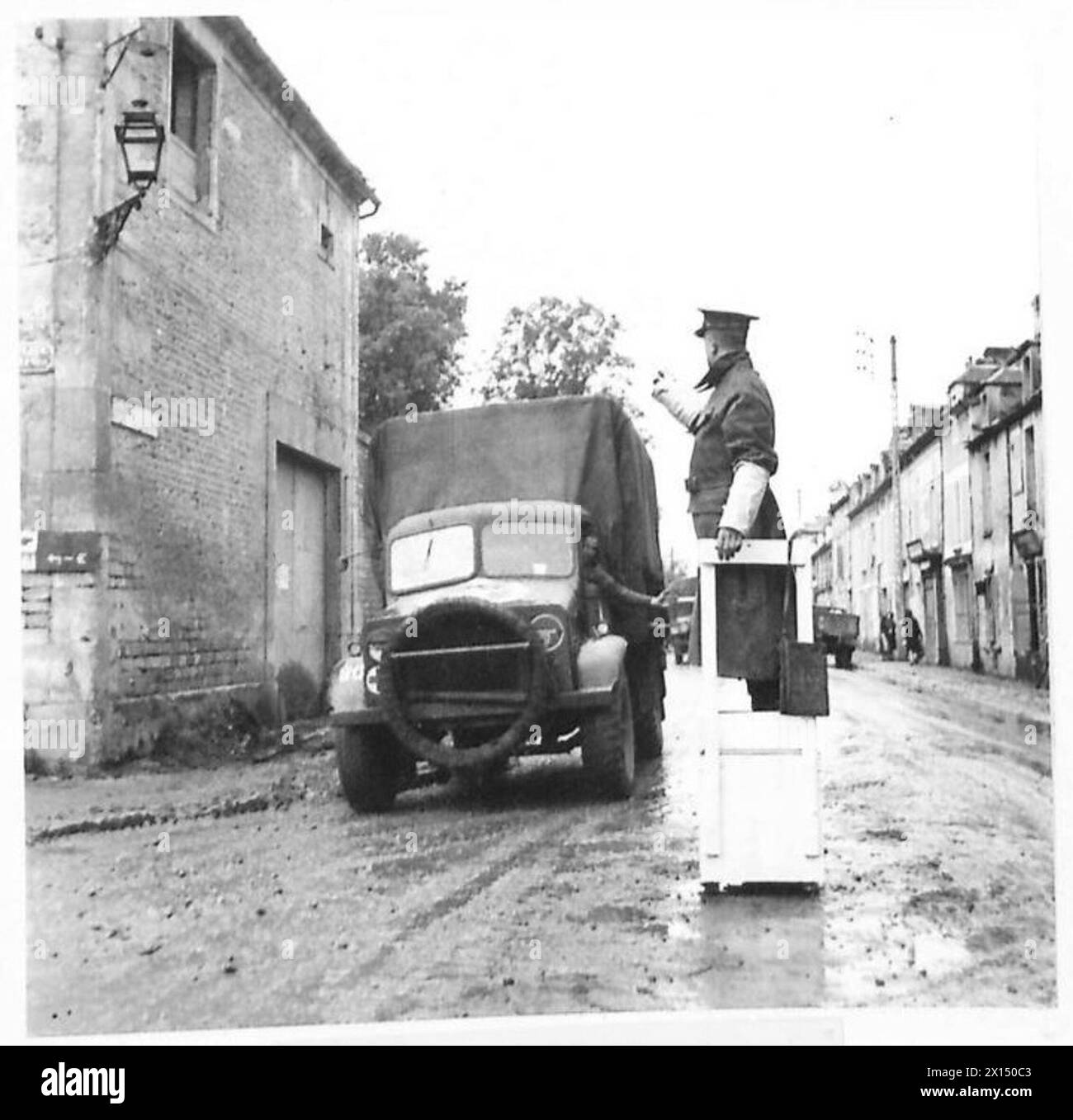 Un policier militaire britannique dirige la circulation à un carrefour dans le village français de Bretteville l'Orgueilleuse, à l'aide d'une plate-forme improvisée lors de 1944-1945 opérations dans le Nord-Ouest de l'Europe. Banque D'Images