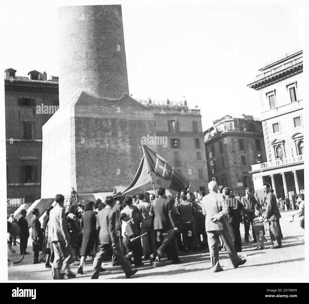 Les civils de la Plaza Colonna, en Italie, portent un drapeau italien avec la colonne Antonio visible en arrière-plan, célébrant pendant les campagnes de l'armée britannique de 1942 à 1946. Banque D'Images